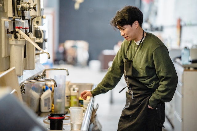 cook in black apron standing by messy sink in kitchen